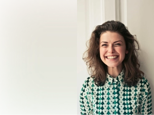 Smiling woman with wavy brown hair wearing a green and white shirt.