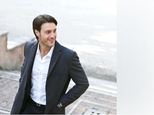 Smiling man with black hair a navy-blue coat and white dress shirt.